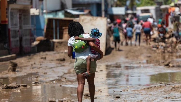 Uma mulher carrega uma criança enquanto caminha por uma rua coberta de lama pelas fortes chuvas, em Leogane, Haiti, 06 de junho de 2023. As fortes chuvas registradas no Haiti nos últimos dias deixaram pelo menos 51 mortos, 18 desaparecidos e 140 feridos , informou a Direção de Proteção Civil (DPC) a 06 de junho num relatório que não reflete os efeitos de um sismo registado esta manhã no sudoeste do país. EPA/Johnson Sabin