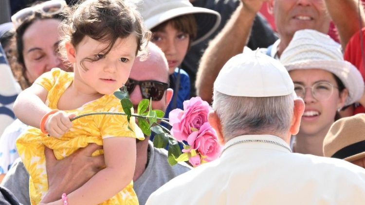 Mãe segura sua filha que oferece flores ao Papa Francisco na Audiência Geral de 28/06/2023