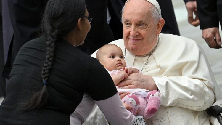Francisco segura uma criança nos braços enquanto vai cumprimentar os fiéis presentes na audiência