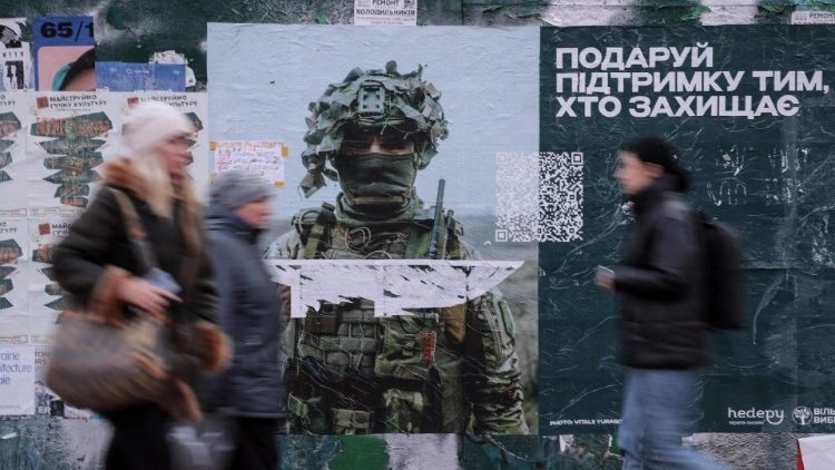 Pessoas passam por um pôster com o retrato de um militar ucraniano em Kiev, Ucrânia, 30 de janeiro de 2024, em meio à invasão russa. As tropas russas entraram em território ucraniano em 24 de fevereiro de 2022, iniciando um conflito armado que provocou destruição e uma crise humanitária. EPA/OLEG PETRASYUK