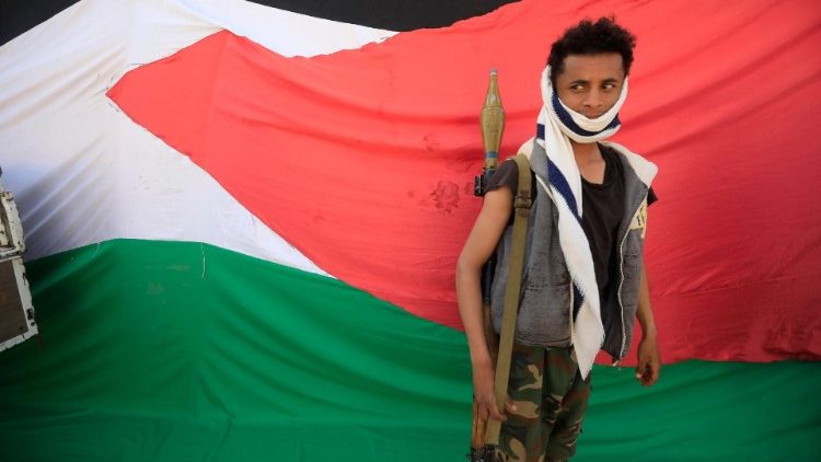 A new Houthi recruit stands in front of a large-scale Palestinian flag, Yemen, 7 February