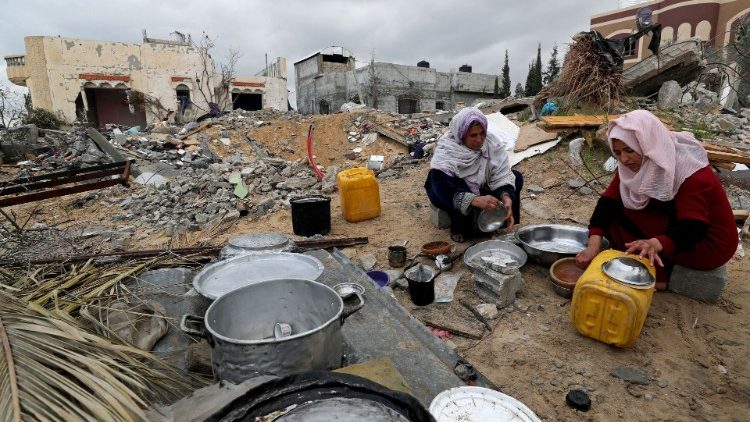 Palestinian women wash utensils at the site of their destroyed house on a cold winter day in Gaza