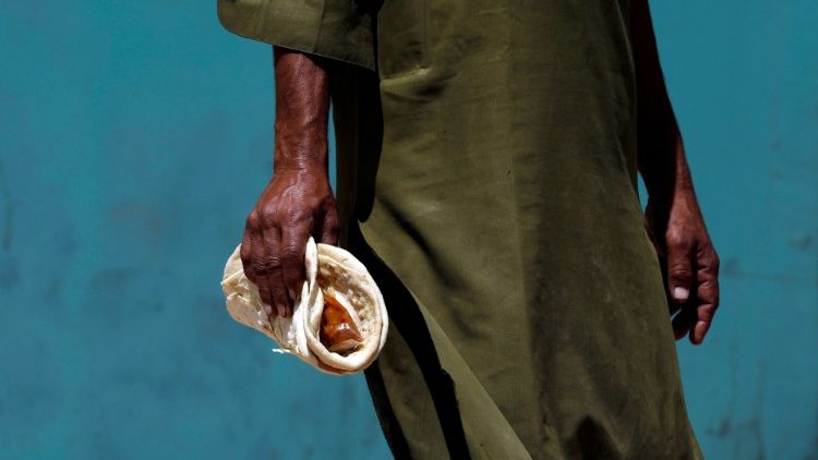 A daily wage labourer in Pakistan holds a handout of traditional bread and curry which he has received from a charity distribution point during covid-19 lockdown
