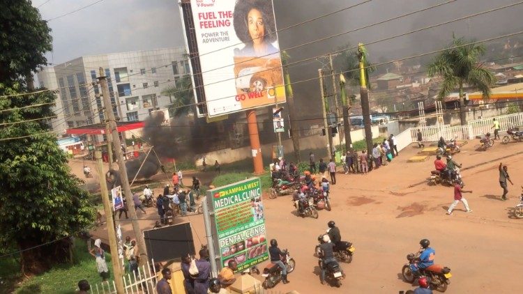 People ride motorcycles as smoke rises from burning objects in a street in Kampala