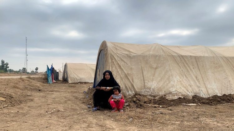 A displaced Iraqi woman and her child sit in front of their tent in an informal camp in the town of Balad
