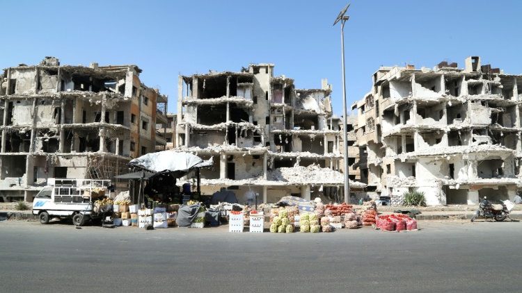 Vegetables are displayed for sale near damaged buildings in Homs, Syria
