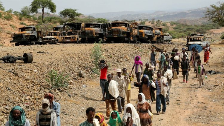 Villagers walking past a line of burnt-out vehicles in Tigray