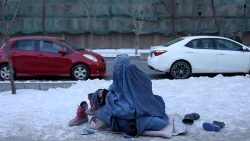 An Afghan woman holding her child begs on a snow-covered pavement in Kabul