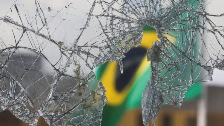 ब्राजील के लोकतंत्र विरोधी दंगों के बाद टूटे ग्लास से दिखता हुआ ब्राजील का झंडा 