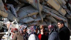 Survivors stand next to rubble at the site of a collapsed building in Kirikhan, Turkey
