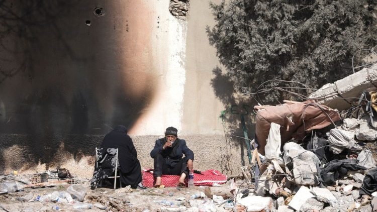 A couple sits next to rubble at the site of a collapsed building in Kahramanmaras, Turkey