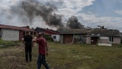 वोवचांस्क शहर में यूक्रेन-रूस सीमा के पास गोलाबारी के बाद धुआं उठते समय स्थानीय निवासी वहीं मौजूद हैं