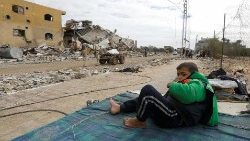 A Palestinian boy rests on mattress near ruins of his house in Khan Younis