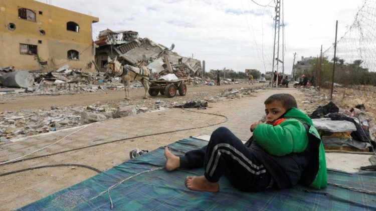 A Palestinian boy rests on mattress near ruins of his house in Khan Younis