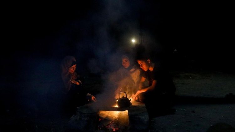 A displaced Palestinian woman sits with her children around a fire, in Khan Younis