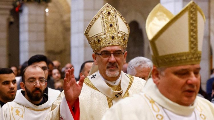 Kardinal Pizzaballa, mittig mit erhobener Hand, in Bethlehem; vor ihm im Bild Kardinal Krajewski