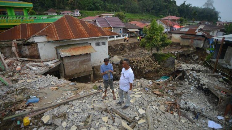 तनाह दातार में बाढ़ से प्रभावित क्षेत्र के एक क्षतिग्रस्त घर के पास खड़े लोग
