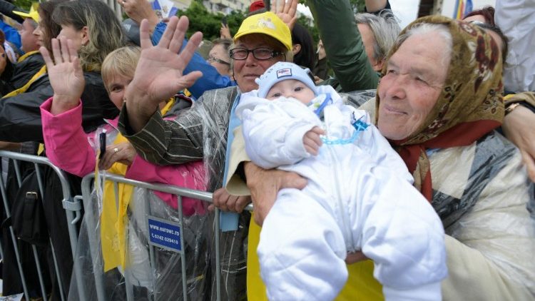 An elderly woman holds her grandchild up for Pope Francis in Romania