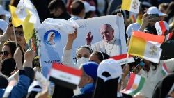 Des fidèles rassemblés au stade d'Erbil brandissent une photo du Pape, au milieu des drapeaux du Vatican, de l'Irak et du Kurdistan irakien.