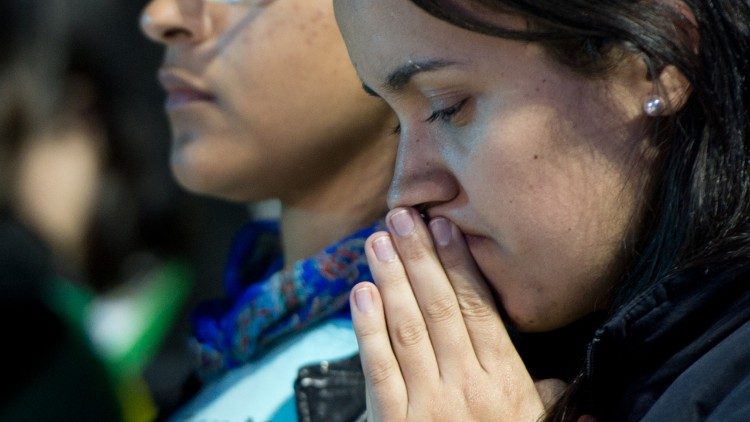 Fiatal katolikus hívő imára kulcsolt kézzel