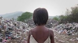 A little girl walks amid mountains of trash