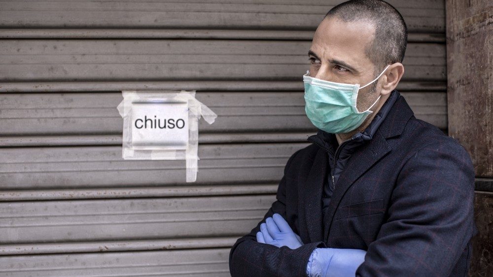 Un uomo rasato  con mascherina giacca e guanti è sconschiude la  serranda  della sua attività a causa delle restrizioni per la pandemia., 