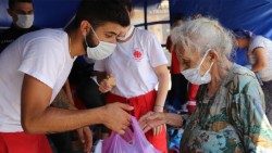 Un'anziana libanese riceve un pacco alimentare a Beirut da un volontario della Caritas locale