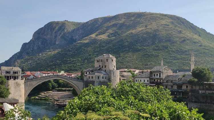 The old bridge of Mostar with two mosques on the right and a cross on the hill