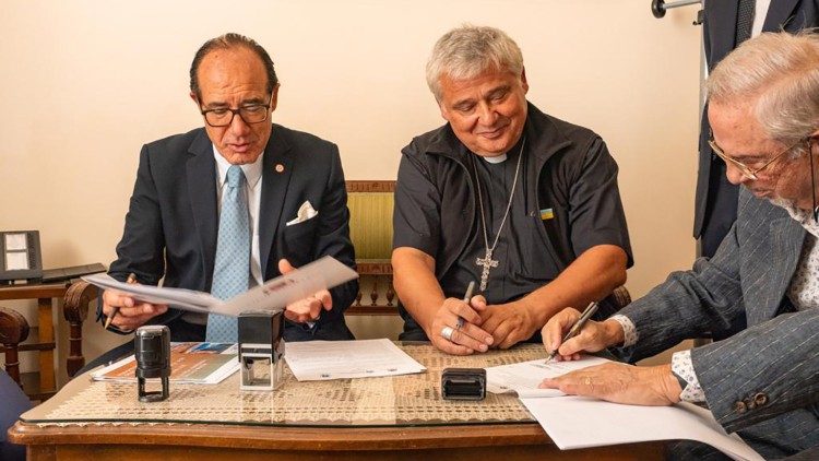  O cardeal Krajewski assina o acordo com o professor Profita (à esquerda), o reitor da universidade UniCamillus, e o dr. Nicolò Vinciguerra (à direita), da clínica "Madonna della Fiducia"