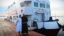 A Ir. Márcia Lopes Assis em frente ao “Barco-Hospital Papa Francisco”, com frei Afonso Lambert