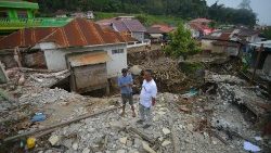 तनाह दातार में बाढ़ से प्रभावित क्षेत्र के एक क्षतिग्रस्त घर के पास खड़े लोग